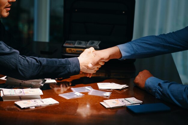 Photo cropped image of drug dealer and buyer shaking hands over table with money and small bags with tablets