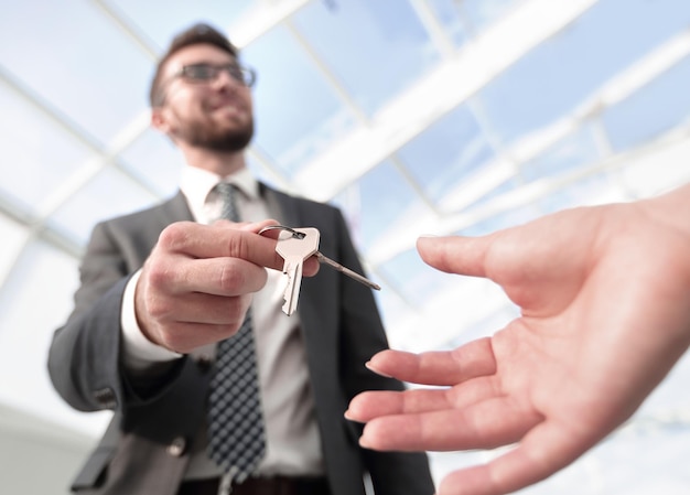 Обрезанное изображение агента по недвижимости, дающего ключи от дома мужчине в офисе