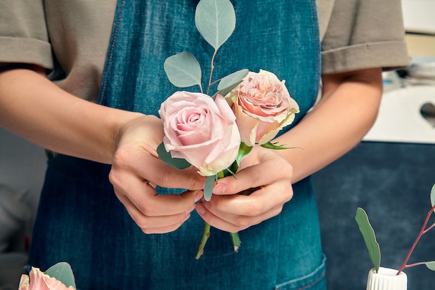 Photo cropped image of female florist at work. arranging various flowers in bouquet. close up flowers in hand. florist workplace. floral, decoration studio. professional concept. copy space for design