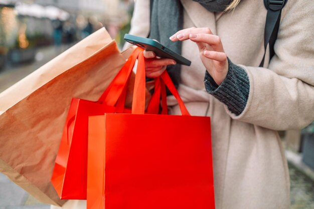 Cropped image of female hands holding red holiday gifts packages used phone on the city street near