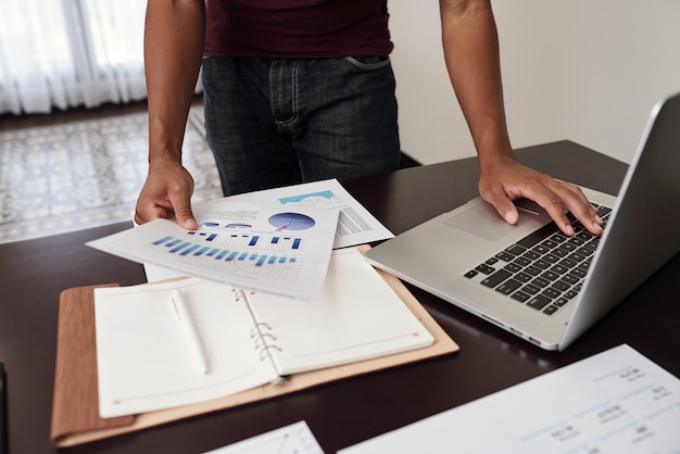 Cropped image of financial analyst checking reports with charts and diagrams on his desk