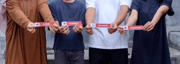 Photo cropped image of four young people showing printed paper with like, comment, share, and subscribe te