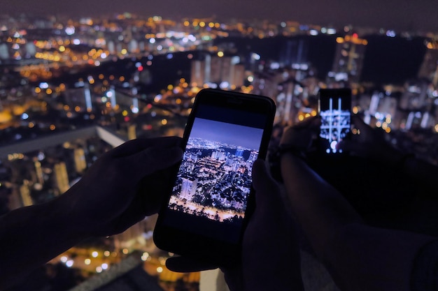 Cropped image of friends photographing illuminated cityscape through smart phone