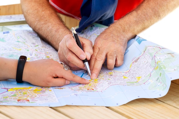 Photo cropped image of friends pointing on map at table