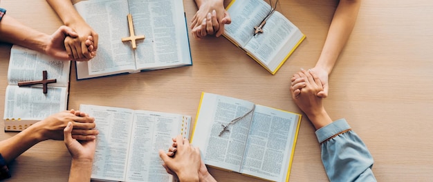 Cropped image of group of people praying together while holding hand on holy bible book at wooden church Concept of hope religion faith christianity and god blessing Top view Burgeoning