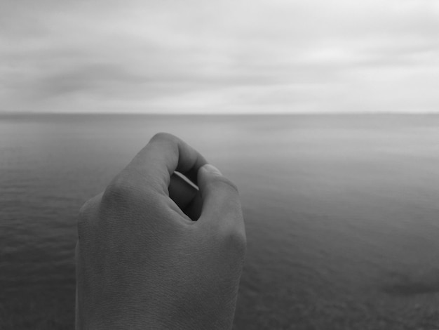 Photo cropped image of hand against sea at beach