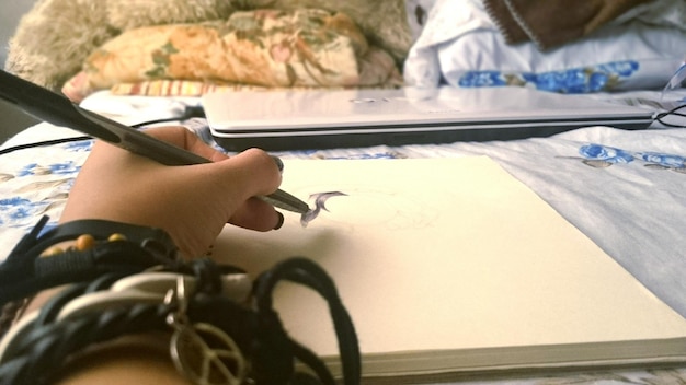 Cropped image of hand drawing in book on bed