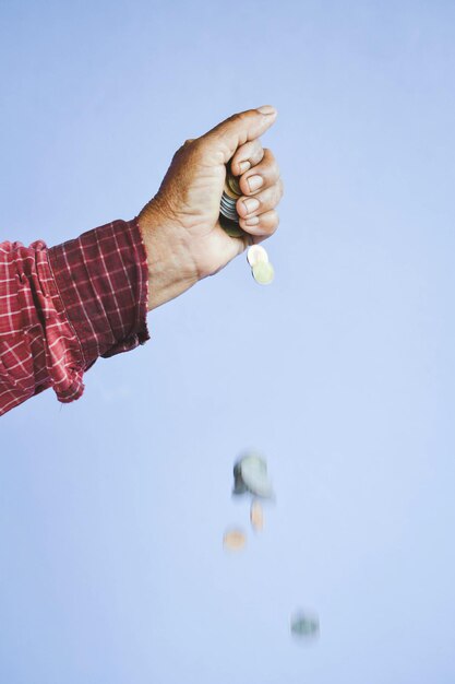 Cropped image of hand dropping coins against purple background