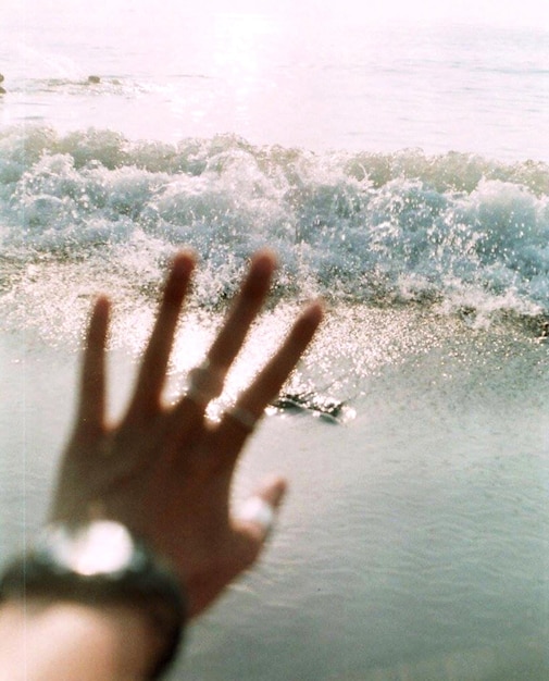 Photo cropped image of hand on glass window against waves in sea