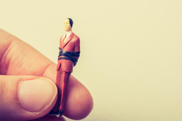 Photo cropped image of hand holding figurine against beige background