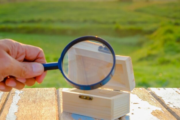 Foto immagine ritagliata di mano che tiene una lente d'ingrandimento su una scatola di legno sul tavolo