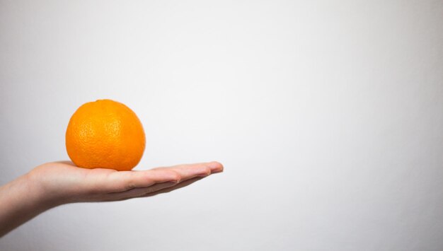 Cropped image of hand holding orange against white background