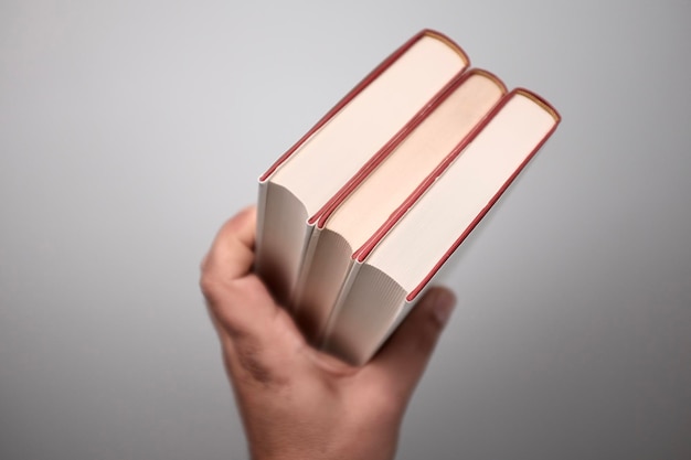 Обрезанное изображение руки, держащей три книги у стены