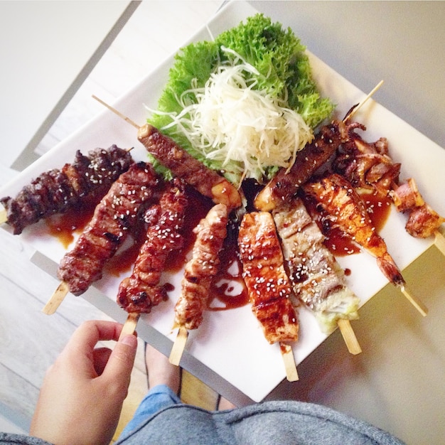 cropped image of hand holding yakitori on table