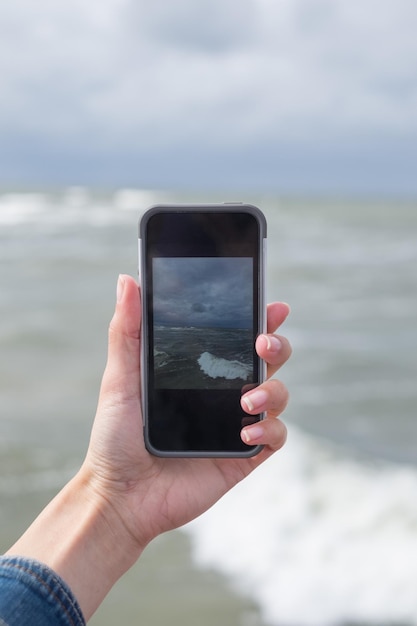 Photo cropped image of hand photographing sea through mobile phone