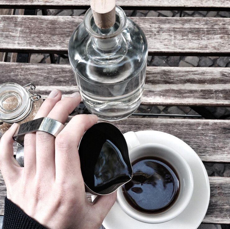Photo cropped image of hand pouring black coffee at table