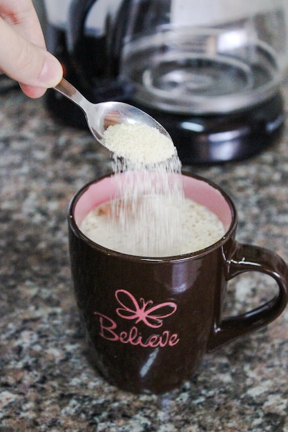 Foto immagine ritagliata di una mano che versa lo zucchero in un cappuccino