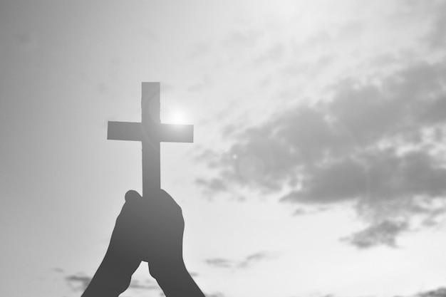 Photo cropped image of hands holding cross against sky during sunset