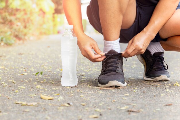 Immagine ritagliata delle mani che lega i lacci delle scarpe alla sneaker con l'acqua in bottiglia.