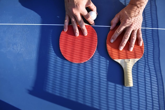 cropped image of hands with tennis rackets and ball on table