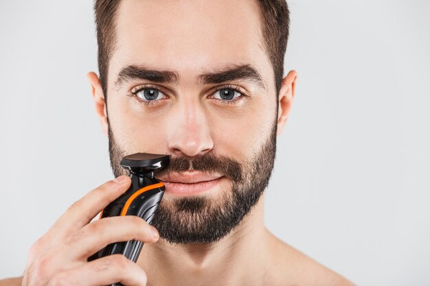 Foto immagine ritagliata di un bell'uomo barbuto che si rade con un rasoio elettrico isolato sopra bianco