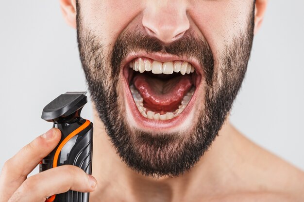 Cropped image of a handsome bearded man shaving with an electric razor isolated over white