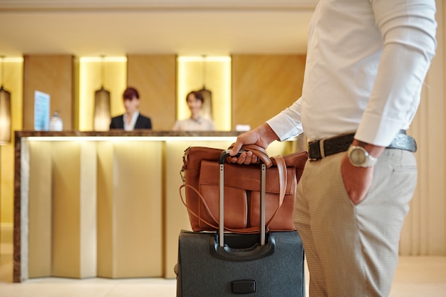 Cropped image of hotel guest standing in lobby with luggage after checking in