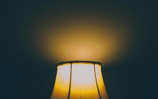 Photo cropped image of illuminated lamp shade against wall in dark