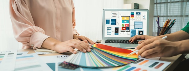 Cropped image of interior designer chooses color from color swatches while laptop displayed UI and UX designs for mobiles app and website Creative design and business concept Variegated
