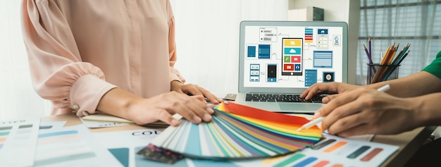 インテリアデザイナーがカラースワッチからカラーを選択し,ラップトップがモバイルアプリとウェブサイトのためのUIとUXデザインを表示します. クリエイティブなデザインとビジネスコンセプト