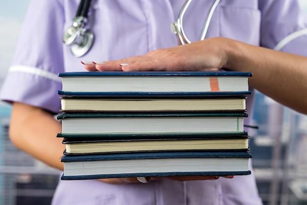 Cropped image of intern in med uniform holding many books in front of her in hospital