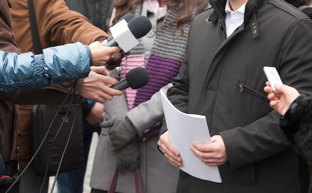 Foto immagine ritagliata di un giornalista che tiene i microfoni davanti alle persone