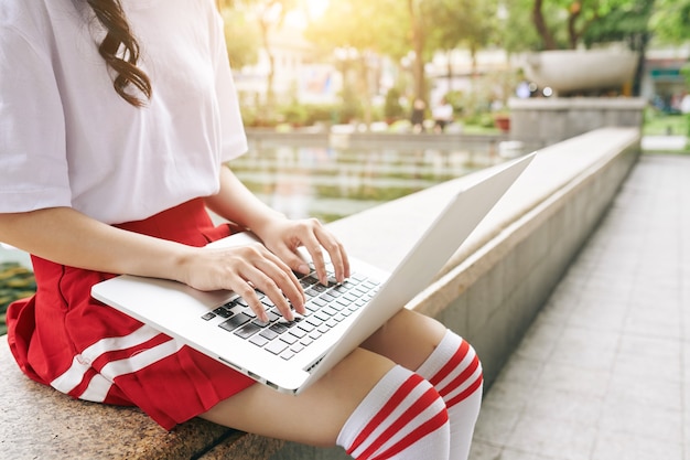 Cropped image of Korean schoolgirl in uniform working on laptop on campus