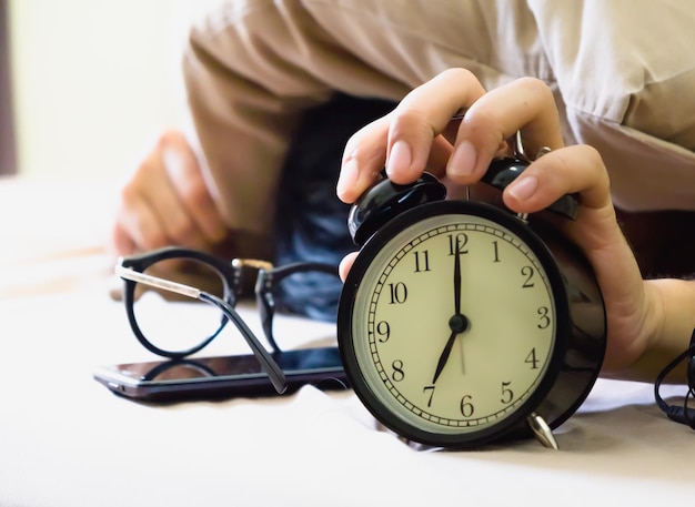 Cropped image of man holding alarm clock on bed