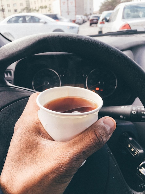 Cropped image of man holding coffee cup while driving car