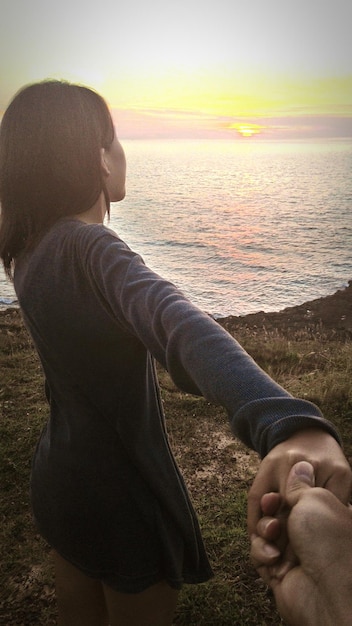 Foto immagine ritagliata di un uomo che tiene la fidanzata sulla spiaggia contro il cielo durante il tramonto