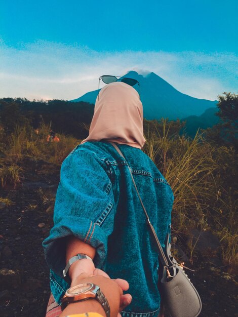 Cropped image of man holding hands with girlfriend on landscape against blue sky