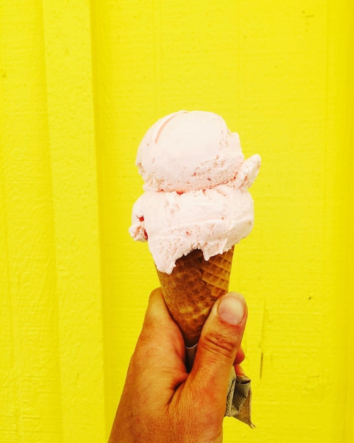 Foto immagine ritagliata di un uomo che tiene un cono di gelato contro una parete gialla