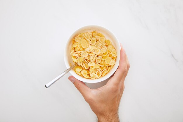 Cropped image of man holding white bowl with cornflakes on marble background