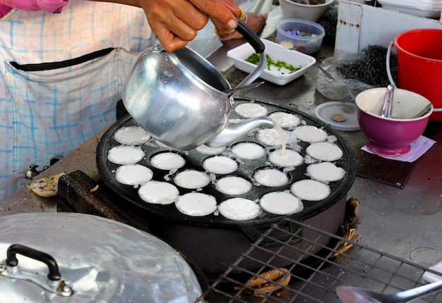 Cropped image of man pouring coconut milk from kettle while cooking kanom krok