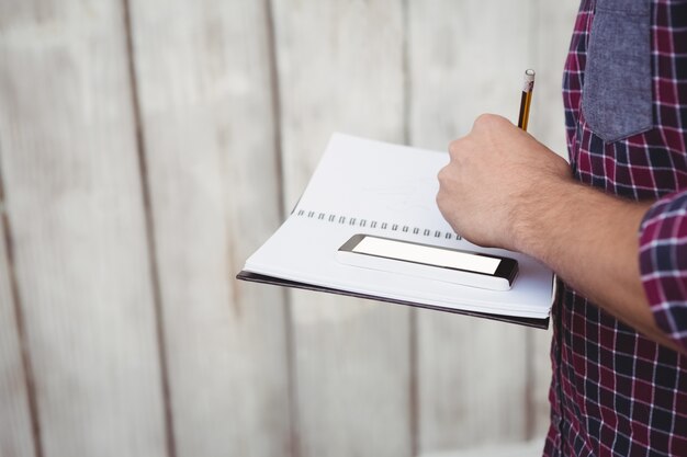 Cropped image of man with smartphone writing on book