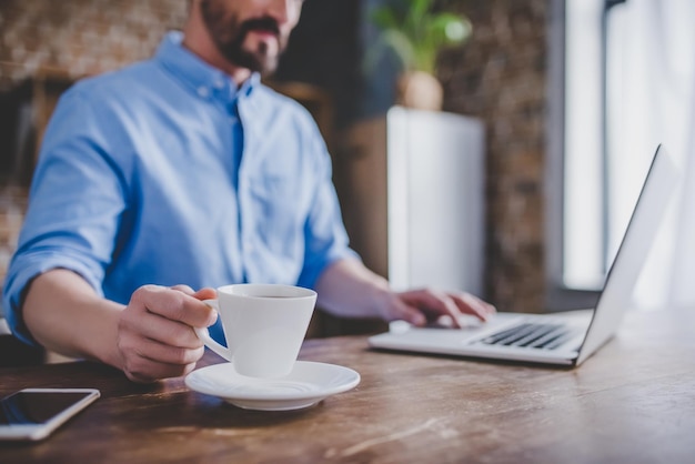 Cropped image of man working on laptop and drinking coffee at the kitchen in the morning