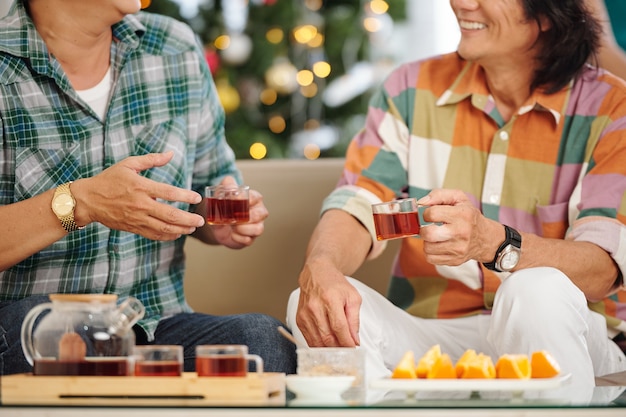 お茶を飲み、ニュースについて話し合い、ハウスパーティーで冗談を言っている成熟したアジア人男性のトリミングされた画像