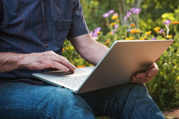 Photo cropped image of a mature man working on his laptop in garden old male blogger typing on notebook