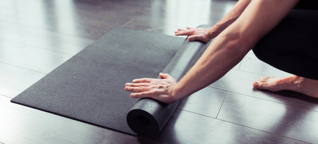 Cropped image of men hands rolling black yoga mat