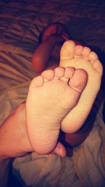 Cropped image of mother holding baby feet on bed at home