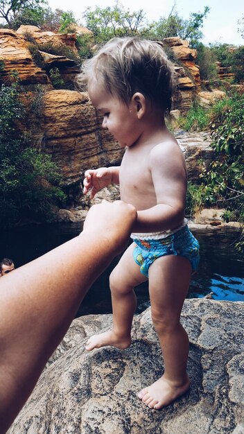 Photo cropped image of mother holding toddler while standing on rock by lake