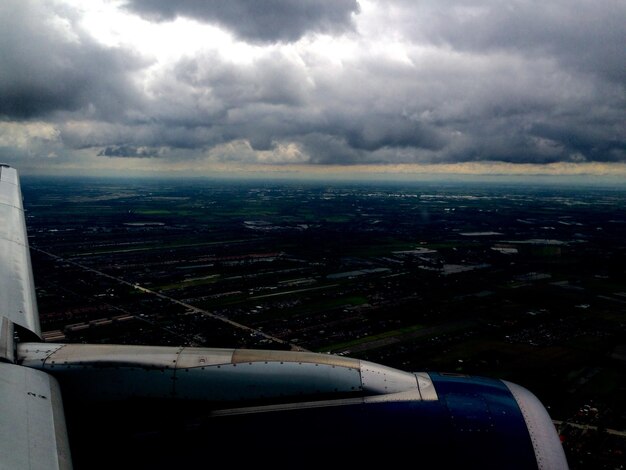 Фото Обрезанное изображение самолета над пейзажем на фоне облачного неба
