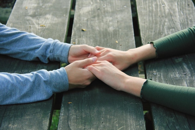 Фото Обрезанное изображение пары, держащейся за руки за деревянным столом