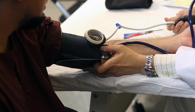 写真 診療所で血圧計とステトスコップで患者の腕を検査している医師のクロップされた画像